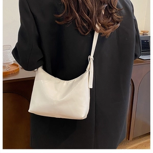 Detail of a creamy white glossy crescent hobo bag with pleated leather texture on model
