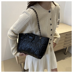 Dettaglio borsa a spalla trapuntata nera con catena, indossata con stile da una modella
