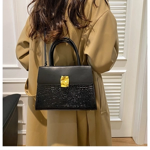 Detail of black handbag showing crocodile embossed texture and golden metal buckle