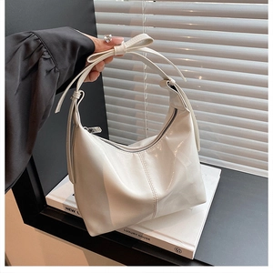 Close-up of white patent leather crescent bag with bow detail and metallic zipper