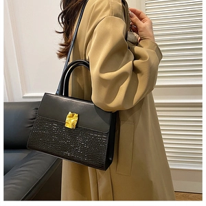 Close-up of black crossbody bag with crocodile texture and gold clasp on khaki coat
