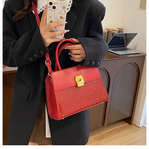 Detail of red crocodile texture handbag with gold buckle held by a model in black blazer