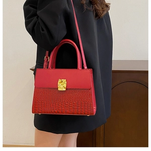 Close-up of red crocodile embossed handbag with golden irregular metal buckle detail