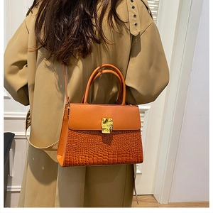 Detail of orange brown crossbody bag with crocodile pattern and golden metal buckle
