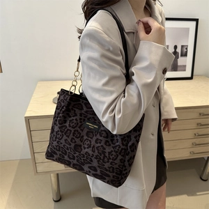 Large leopard print tote bag with gold chain strap carried by a model in a beige blazer