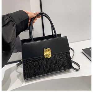 Detail of black crossbody bag with mixed matte and crocodile embossed textures and gold clasp