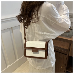 Detail of a vintage two-tone crossbody bag with white croc-embossed texture and brown trim