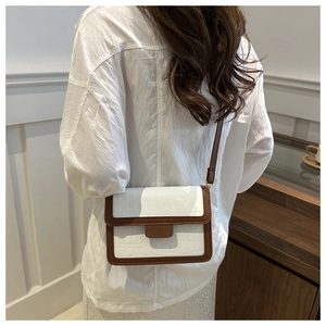 Detail of white crocodile texture crossbody bag with brown leather trim on a model