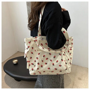 Dettaglio della borsa tote in velluto beige con stampa fragole e tasche laterali