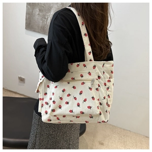 Detail of off-white corduroy tote bag with strawberry pattern worn by model