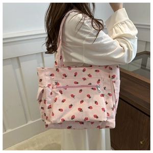Detail of pink corduroy tote bag featuring red strawberry patterns and a front zipper pocket