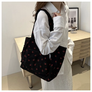 Close-up of black corduroy tote bag featuring red strawberry embroidery and front zip pocket