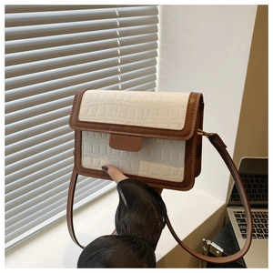 Detail of a brown and white crocodile embossed flap on a structured crossbody bag