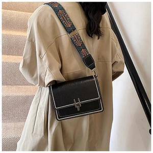 Detail of a black leather square bag with white stitching and colorful ethnic strap