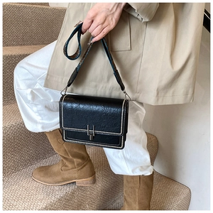 Detail of vintage black leather bag with pearl studs and jacquard strap on a trench coat