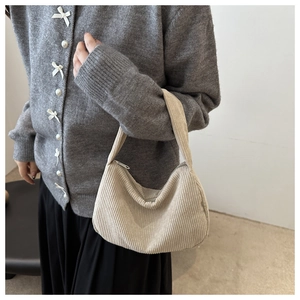 Close-up of beige corduroy underarm bag styled with a grey cardigan and black skirt