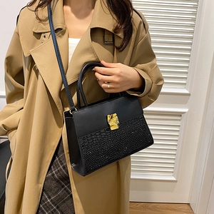 Elegant black crossbody bag with faux crocodile texture and gold clasp on a trench coat