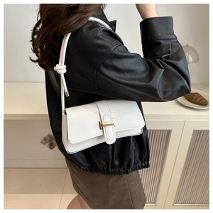 Side view of a white minimalist shoulder bag with gold clasp on a model in leather jacket