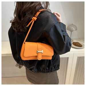 Detail of orange square shoulder bag with gold clasp and decorative knot strap