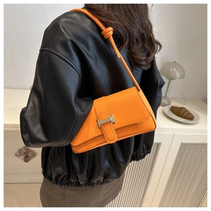 Detail of vibrant orange baguette bag with H-shaped metal buckle on a dark leather jacket