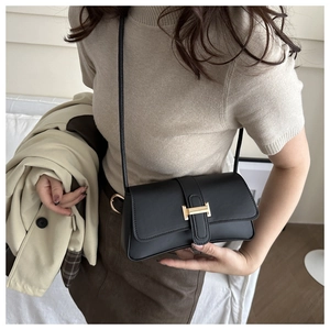Detail of a chic black leather crossbody bag with a distinctive golden metal buckle clasp