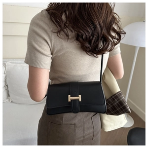Detail shot of a black matte crossbody bag with rectangular gold metal buckle closure