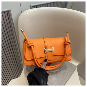 Chic orange baguette shoulder bag with gold metal buckle and knotted strap on books