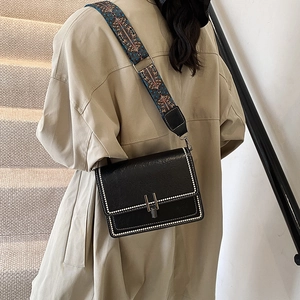 Vintage black crossbody bag with colorful woven strap worn by a woman in a trench coat
