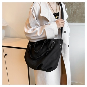 Detail of black canvas tote bag with metal grommets and detachable strap on a model