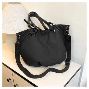 Detail of black canvas tote bag showing leather handles and gunmetal hardware accents