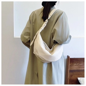 Minimalist beige crescent crossbody bag worn with a khaki trench coat in a clean interior