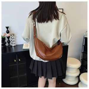 Brown leather crescent bag worn crossbody with adjustable wide strap by a model