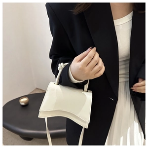 Detail of white geometric leather handbag showing unique curved bottom and slim strap