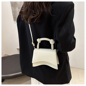 Close-up of beige hourglass mini bag with knot handle worn over a black blazer