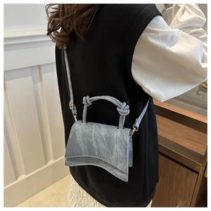 Detail of light blue denim textured crossbody bag with unique curved base on model