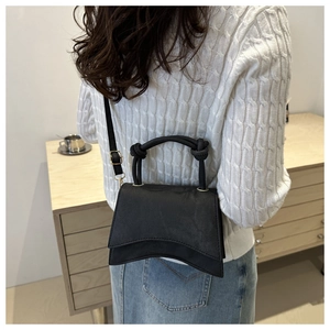 Detail of black matte leather shoulder bag with unique curved base and knotted handle straps