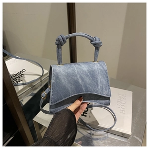 Detail of blue denim mini bag featuring a unique knotted handle and gold metal hardware