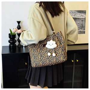 Detail of leopard print tote bag featuring a plush cloud charm and brown leather strap