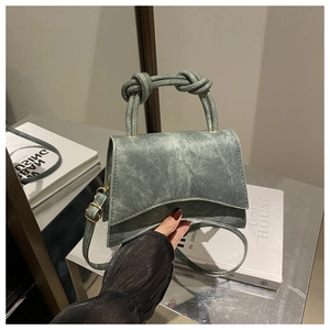 Detail of green denim crossbody bag with twisted handle and asymmetrical curved bottom