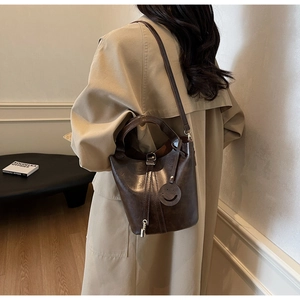 Detail of dark brown glossy bucket bag with silver lock and smiley charm on model