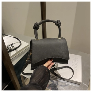 Detail of black trapezoid handbag with knotted handle and matte texture finish