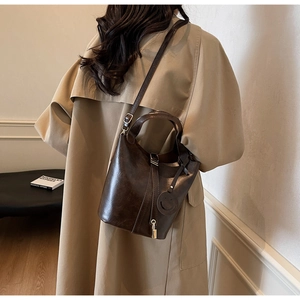 Détail d'un sac seau en similicuir marron foncé avec poignée et breloque visage souriant