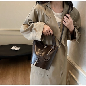 Sac seau marron en cuir huilé avec breloque sourire et fermoir doré porté sur un trench-coat