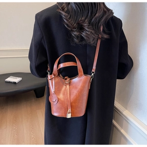 Détail du sac seau caramel avec fermoir métallique et pendentif smiley sur un mannequin