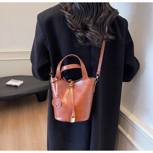 Sac seau en cuir marron avec bandoulière réglable et cadenas porté par un mannequin