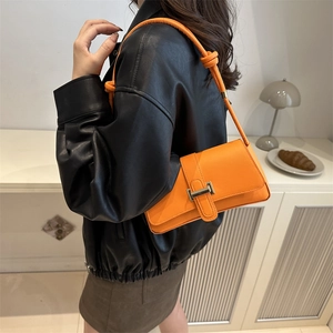 Orange leather crossbody bag with silver buckle and knotted strap on model in a home setting