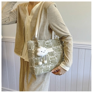 Close-up of green woven tote bag with white straps and cute plush cloud pendant