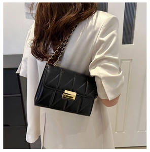Détail d'un sac bandoulière matelassé noir avec chaîne et boucle dorées sur un mannequin
