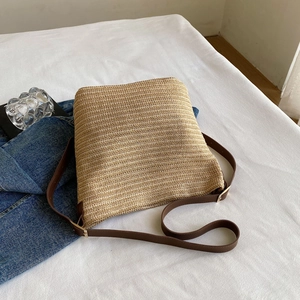 Close-up of woven straw bag detail featuring brown leather strap and gold hardware accents