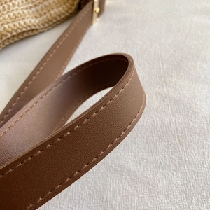 Detail of brown leather shoulder strap with fine texture and durable stitching on straw bag